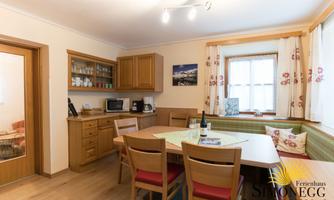 A cozy kitchen with wooden cabinets and a large dining area. A bottle of wine is on the table and the windows are decorated with curtains.