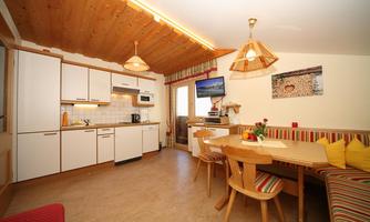 A cozy kitchen with a dining area and wooden ceiling. The equipment includes a modern stove, a television, and an inviting seating area.