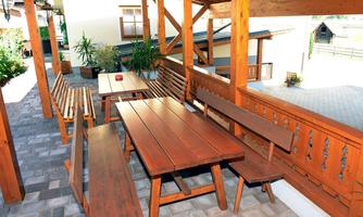 A cozy terrace with wooden furniture and a paved floor. The surroundings are bright and inviting with green plants.