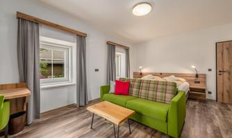 A modern room with a cozy green sofa and a wooden table. Large windows provide plenty of daylight and an inviting atmosphere.