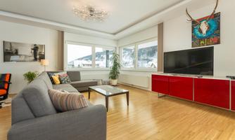 A modern living room with a cozy couch, a large TV, and a stylish table. The colorful walls and large windows provide plenty of brightness and a pleasant stay.
