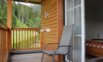 A balcony with a chair and a view of wooded mountains. The wooden paneling gives the room a cozy atmosphere.