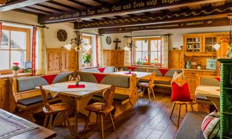 A cozy dining area with wooden furniture and red accents. Large windows let in plenty of daylight, creating an inviting atmosphere in the room.