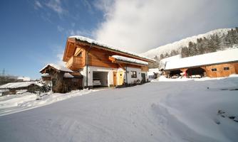A snow-covered chalet in the mountains, surrounded by snow-covered trees. The sky is clear with some clouds.