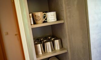 A shelf compartment with various cups and metal mugs. The cups are arranged in different colors and designs.
