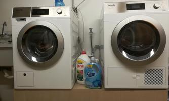 Two modern washing machines stand side by side in a laundry room. Next to them are bottles of detergent.