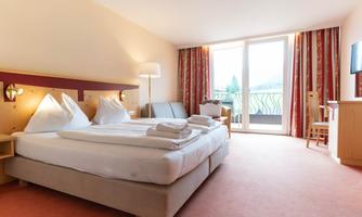 A bright hotel room with a double bed and two pillows. The room features a balcony and a modern television.