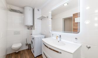 A modern bathroom with bright tiles and a washing machine space. The illuminated mirror and wood surfaces give the room an inviting atmosphere.