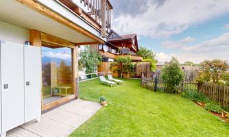 A beautiful garden with well-maintained grass and deck chairs. In the background, there is a modern building and a landscape with trees.