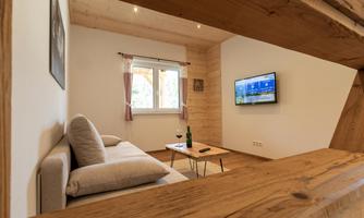 A cozy living area with a modern sofa and a TV on the wall. The room has light walls and wooden details that create a warm atmosphere.