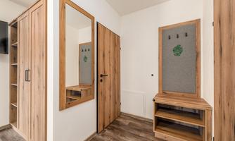 A modern entrance area with wooden shelves and a large mirror. The walls are brightly painted, and there is a practical coat rack.