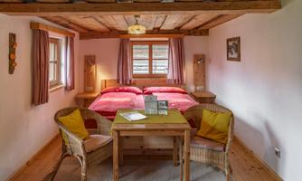 A cozy bedroom with two beds, a small table, and chairs. The walls are bright, and the decor has a rustic wooden style.