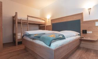 A cozy bedroom with a double bed and a bunk bed. The wooden ceiling and warm colors create an inviting atmosphere.