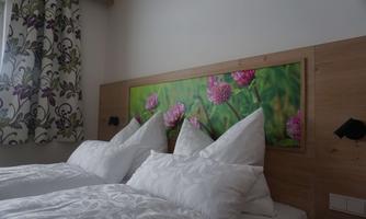 A cozy bedroom with two beds and elegant cushions. In the background, there is a decorative picture of pink flowers.