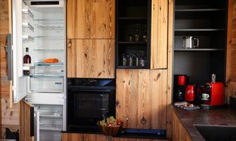 A modern kitchen with wood paneling, featuring an open refrigerator and a stove. Several kitchen appliances and a fruit bowl are on the countertop.