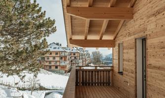 A balcony with wooden cladding and a view of a snowy garden. In the background, several wooden buildings can be seen.