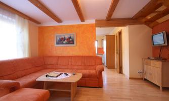 A cozy living space with an orange couch and a wooden table. The walls are painted orange, and there is a television on the wall.