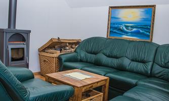 A cozy living room with a green couch and a wood stove. A picture of a maritime landscape hangs on the wall.