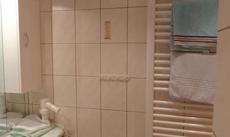 A modern bathroom with white tiles and a sink. Towels hang on a towel warmer, and there is a mirrored cabinet.