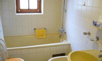 A simple bathroom with a bathtub, a sink, and a toilet. A window allows natural light in, and a yellow towel hangs on the wall.
