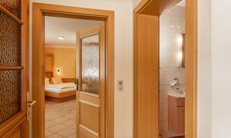 An inviting hallway with wooden doors leading to a bedroom and a bathroom. The bedroom is bright and furnished with a double bed.