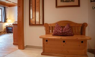 An inviting entryway with a wooden bench and two decorative cushions. The walls are light, and a mirror reflects the space.