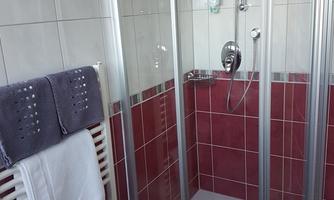 A modern bathroom with a glass shower cabin. The walls are tiled and designed in shades of red and gray.