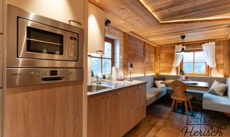 A modern kitchen in a wooden house with warm light. The dining area is cozy and inviting, with a large window and comfortable seating.
