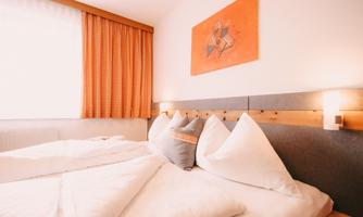 A cozy bedroom with two beds and white bedspreads. An orange artwork hangs on the wall, and the room has bright curtains.