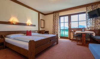 A cozy hotel room with a double bed and a table. Large windows provide a view outside and ensure plenty of light.