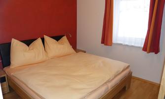 A cozy bedroom with a large bed and red walls. The window lets in a lot of light and the curtains add a warm touch.