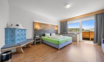 A modern bedroom with a large window and a view of the mountains. There is a comfortable bed, a desk, and a stylish wooden wardrobe.