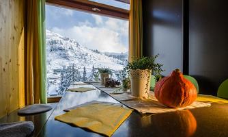 A cozy kitchen table with a pumpkin and a plant. Through the window, you can see a snowy landscape with mountains and trees.