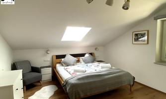 A cozy bedroom with a large bed and two nightstands. The bright atmosphere is emphasized by the skylight and the subtle decor.