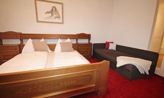 A cozy bedroom with a large bed and a sofa. The walls are light and there is a piece of artwork that lightens the atmosphere.