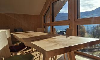 A bright dining area with a large wooden table and many chairs. The large windows offer a beautiful view of the mountains and nature.