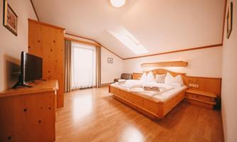 A cozy bedroom with a large double bed and wooden furniture. The room has a large window area that lets in plenty of daylight.