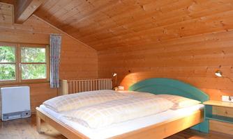 A cozy bedroom with wood paneling and a large double bed. The windows let in plenty of daylight and create a warm atmosphere.