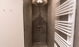 A modern shower with gray walls and an elegant showerhead. On the wall, there is a white towel warmer.