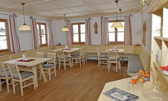A cozy interior with wooden chairs and tables. Bright walls and large windows create an inviting atmosphere.