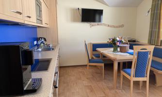 A modern kitchen unit with bright wooden furniture and a blue wall. There are chairs at the table and a vase with flowers.