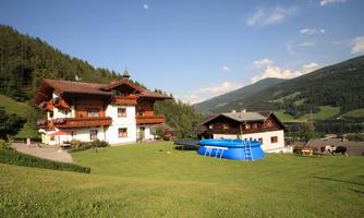 A cozy farmhouse surrounded by green meadows and mountains. In the garden, there is a blue swimming pool.