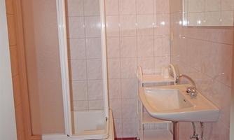 A small bathroom with a shower, a sink, and a toilet. The walls are tiled and the floor has red tiles.