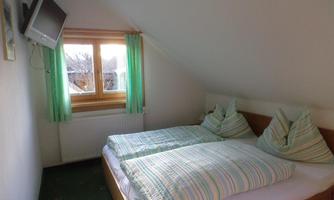A cozy bedroom with two single beds and colorful bedspreads.  
Large windows with green curtains let in plenty of light.