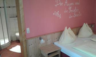 A cozy room with two beds and wooden paneling. A quote is written on the wall and a bathroom can be seen in the background.