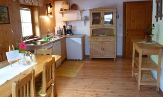 A cozy kitchen with wooden paneling and a dining table. The amenities include a sink, a refrigerator, and a cabinet for dishes.