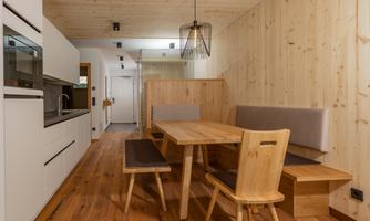 A modern kitchen with a wooden dining table and cozy seating. The walls are made of light wood, creating a warm atmosphere.