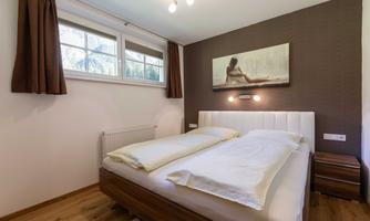A cozy bedroom with a double bed and hardwood floor. The walls are in warm tones, and a large window allows for plenty of natural light.