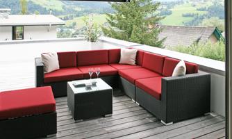A modern terrace with a red sofa and a glass table. The surroundings consist of green hills and trees.