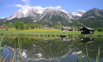 A picturesque landscape with high mountains and green meadows. The clear lake reflects the surroundings.